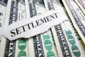A torn paper with the word “settlement” printed on it sits on top of hundred-dollar bills.